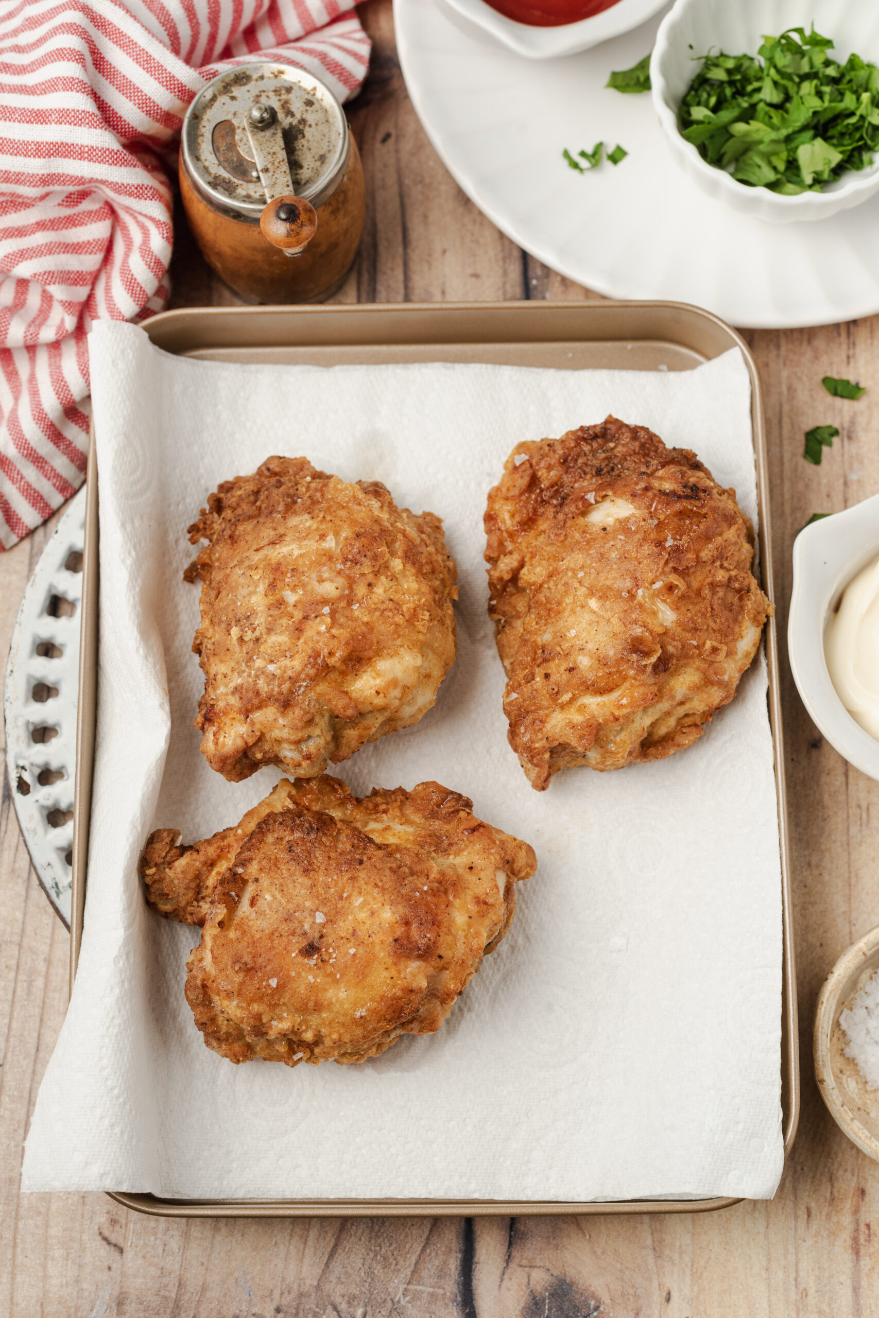 Golden-brown fried chicken pieces draining on paper towels on a baking sheet.