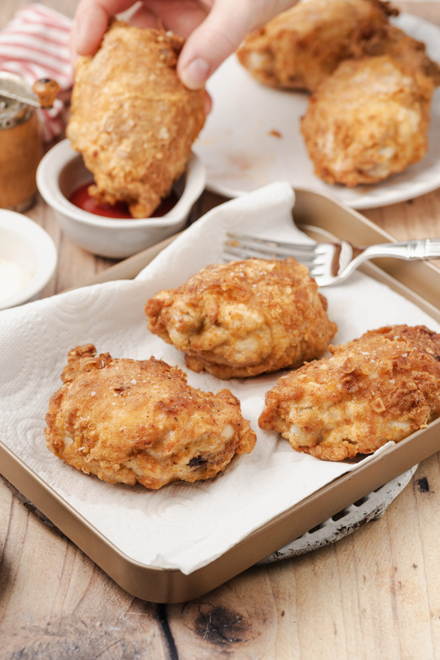 Golden-brown fried chicken pieces on a baking sheet, one being dipped in sauce.