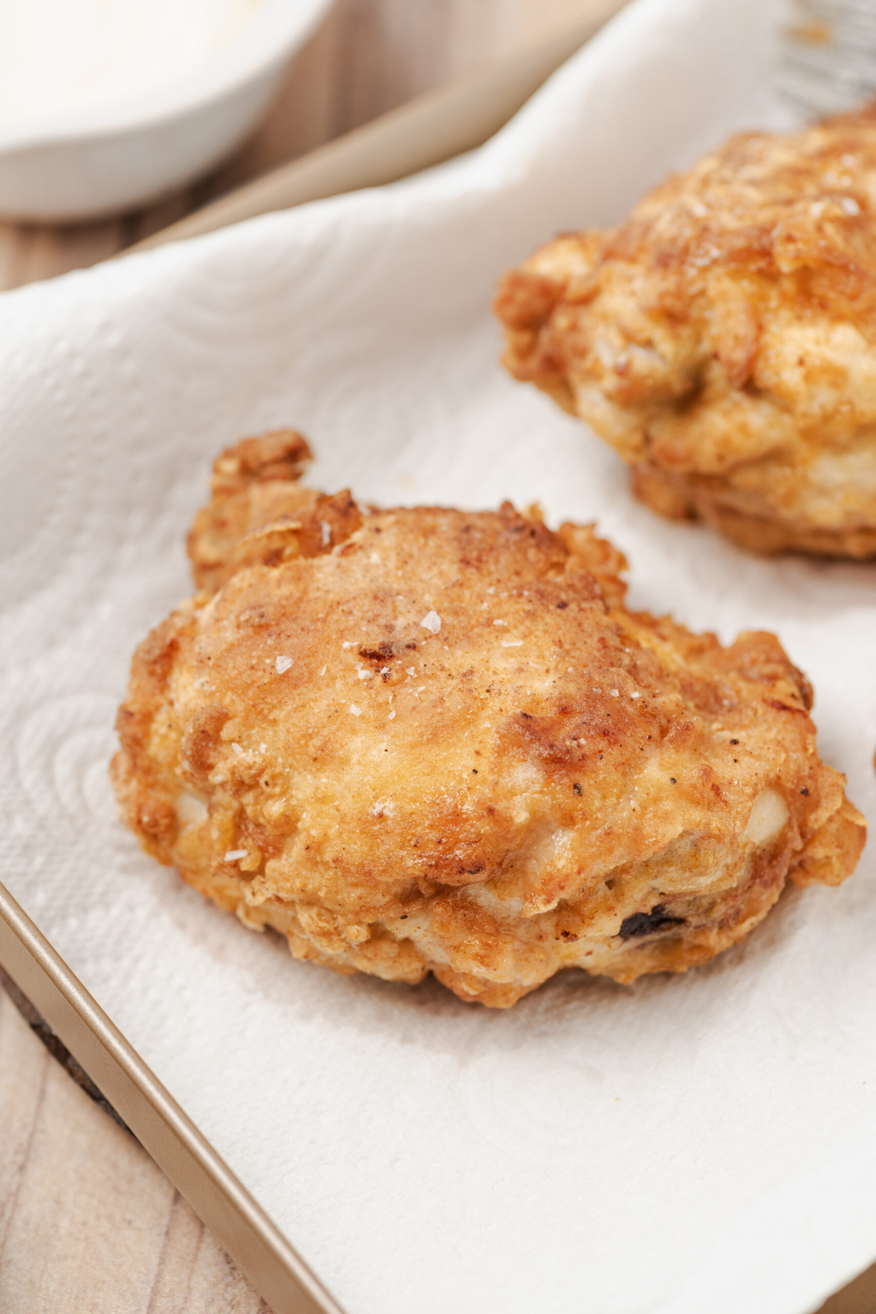 Golden brown fried chicken pieces resting on a paper towel-lined tray, sprinkled with salt.