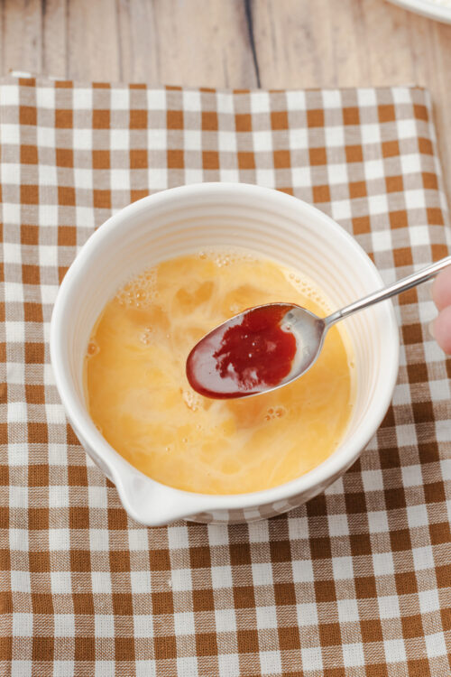 Whisking beaten eggs and hot sauce together in a bowl for fried chicken.