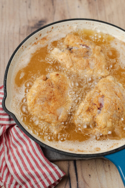 Fried chicken pieces frying in a cast iron skillet.