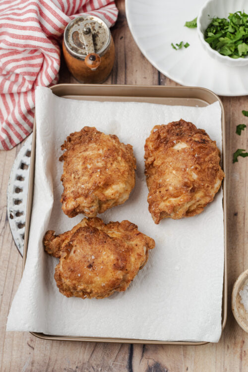 Golden brown fried chicken pieces draining on paper towels.